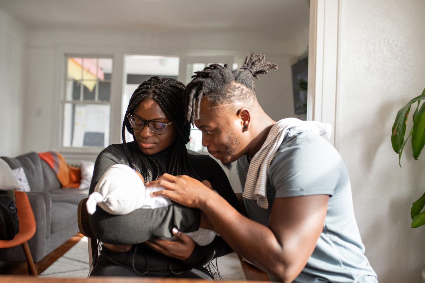 A young couple holding their newborn at the dining table of their apartment.
